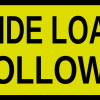 Yellow rounded-corner warning sign that reads 'WIDE LOAD FOLLOWS'